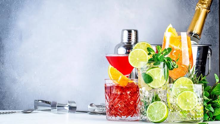 Craft cocktail dalam gelas elegan dengan hiasan buah segar dan bahan aromatik yang diracik bartender di bar modern.